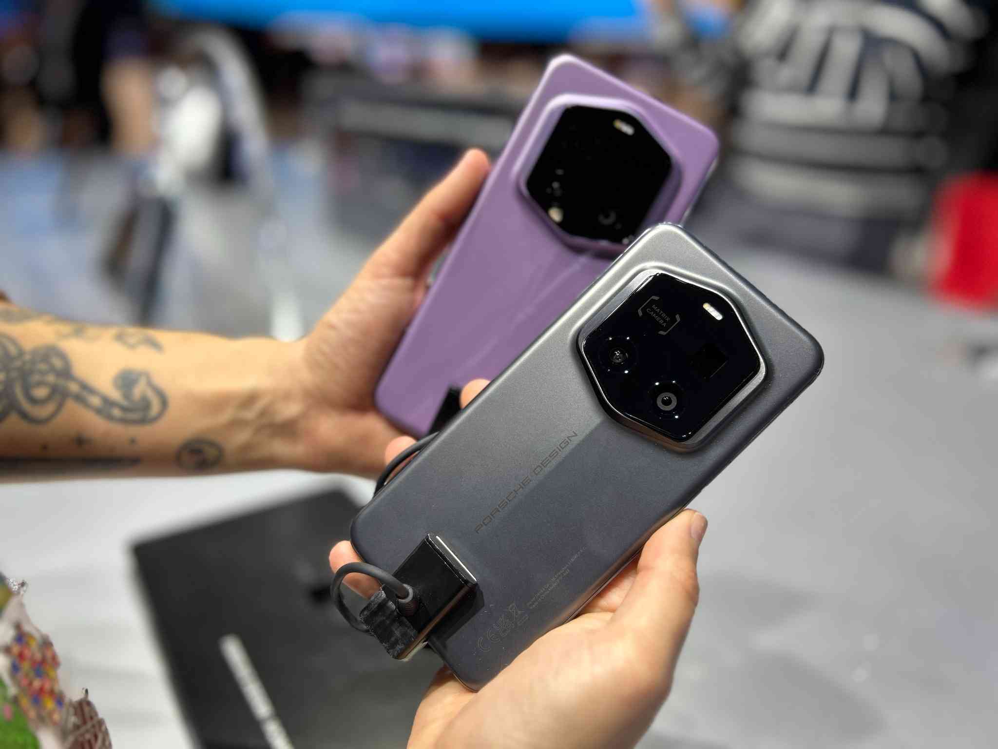 Dos manos sostienen dos teléfonos inteligentes con grandes módulos de cámara negros, uno gris y otro lila.