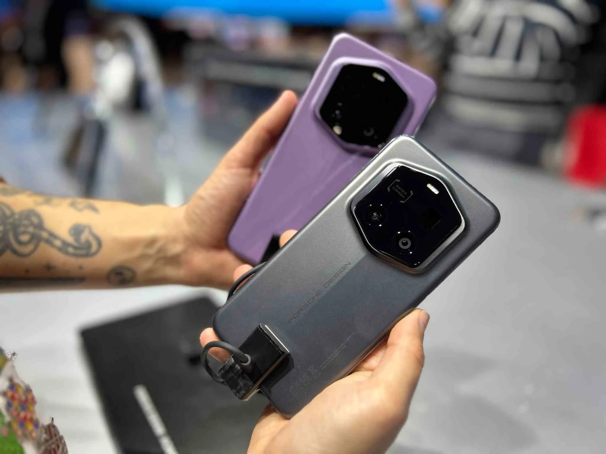 Dos manos sostienen dos teléfonos inteligentes con grandes módulos de cámara negros, uno gris y otro lila.