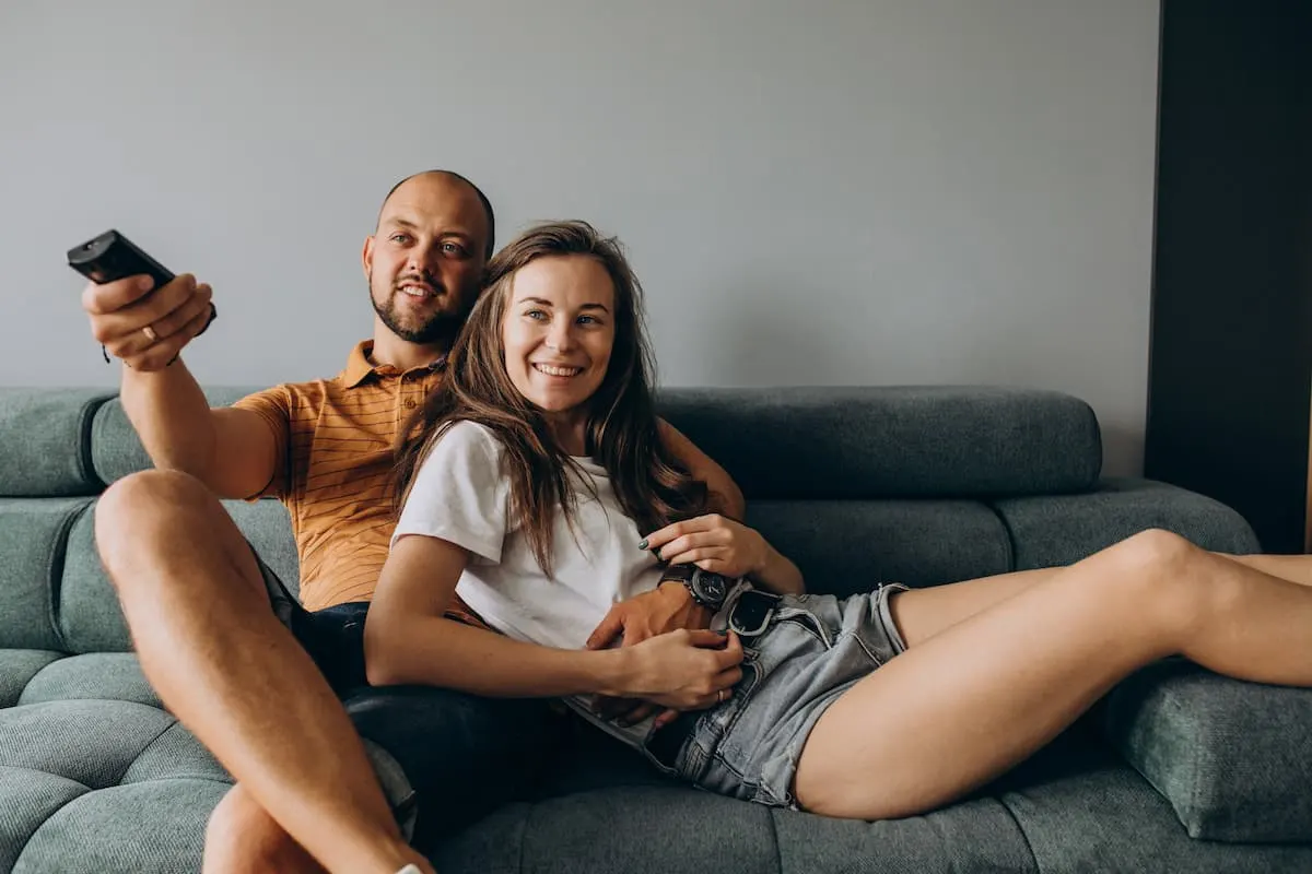 Pareja sonriente viendo la televisión en el sofá.