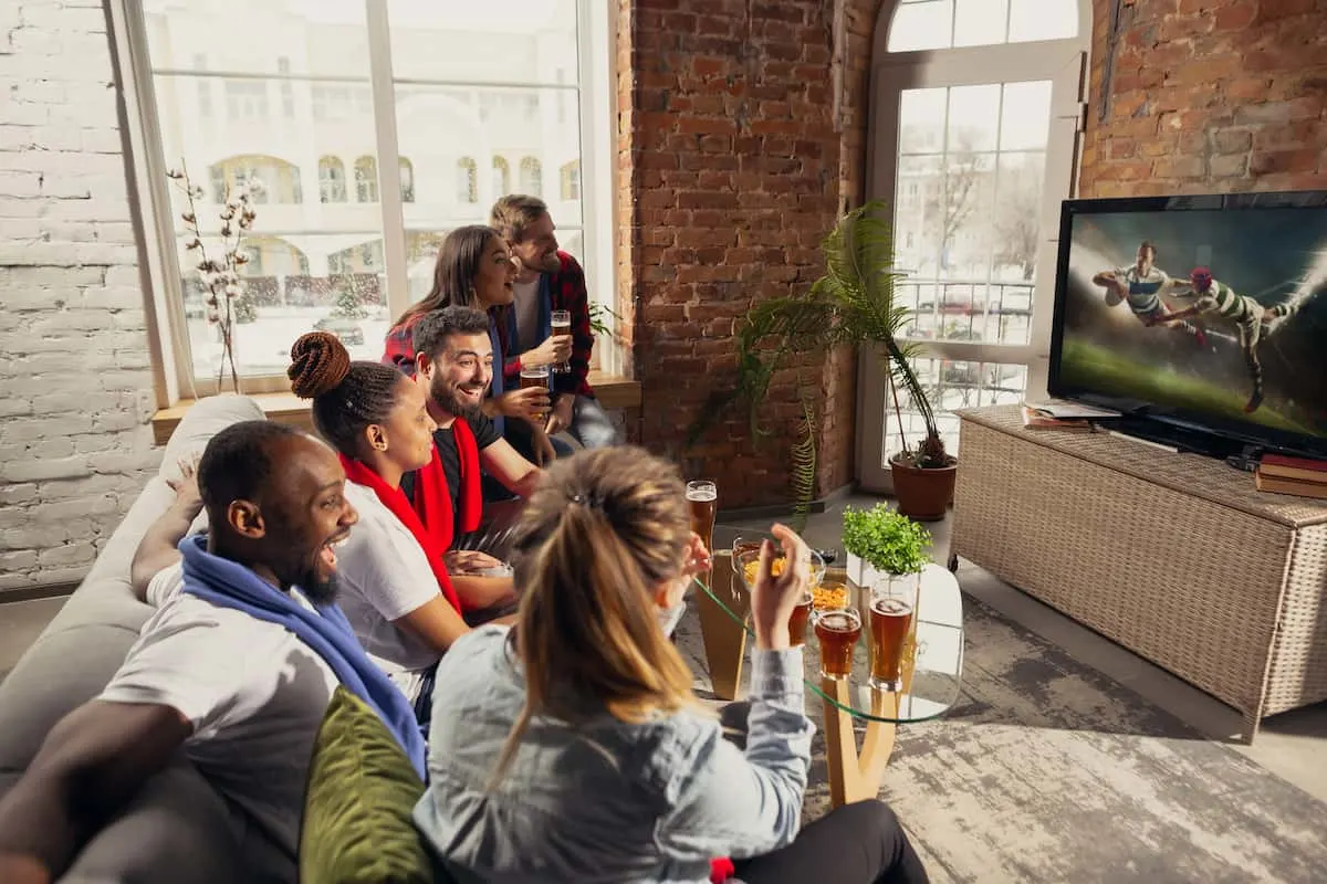 Grupo de amigos viendo un partido de fútbol en televisor en casa con bebidas