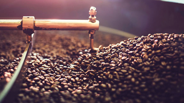 Montón de granos de café tostados con un brazo de metal dorado y una barra encima.