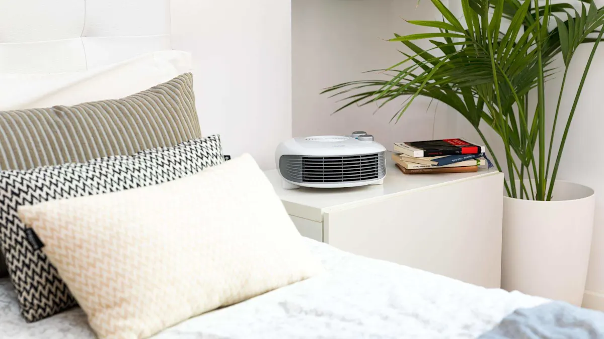 En un dormitorio, una cama con almohadas estampadas y un calentador blanco sobre una mesa, junto a libros y una planta.