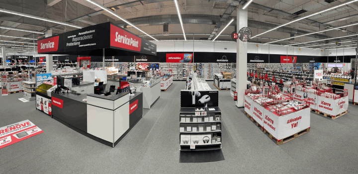 Vista interior de una tienda con estantes llenos de productos, mostradores de servicio en rojo y negro y letreros colgantes.