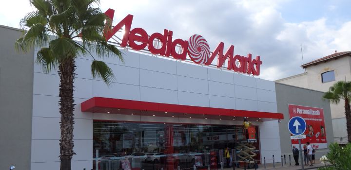 Edificio de Media Markt con letrero rojo, toldo rojo sobre la entrada y palmeras a los lados.