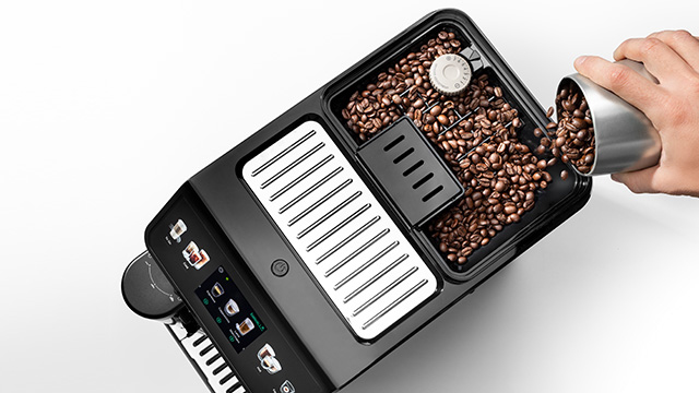 Persona vierte granos de café en una máquina negra. La máquina tiene una pantalla y compartimentos.