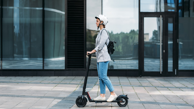 Persona con casco conduciendo un patinete eléctrico por la ciudad.