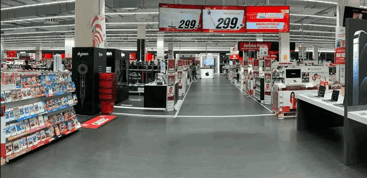 Interior de tienda con estanterías llenas de productos, carteles rojos y blancos colgando del techo.