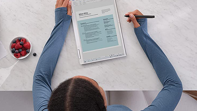 Vista superior de una persona usando una tableta con un lápiz sobre un escritorio blanco con frutas.