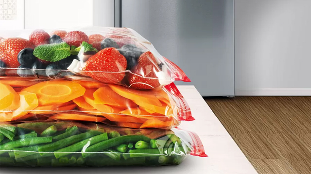 En una mesa frente a un frigorífico, gran cantidad de verduras envasadas al vacío, listas para ser introducidas en el refrigerador