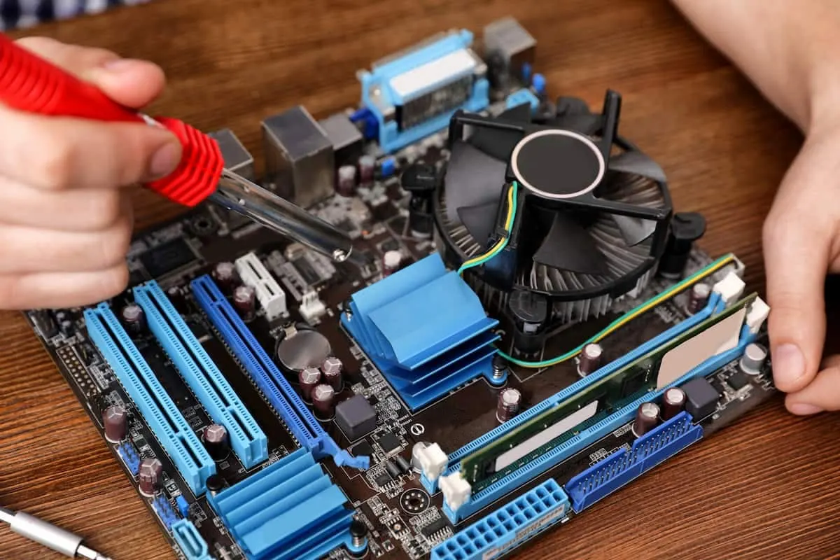 Manos ensamblando componentes en una placa base de computadora con destornillador rojo.