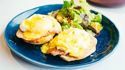 Plato azul con huevos benedictinos y ensalada verde de acompañamiento.