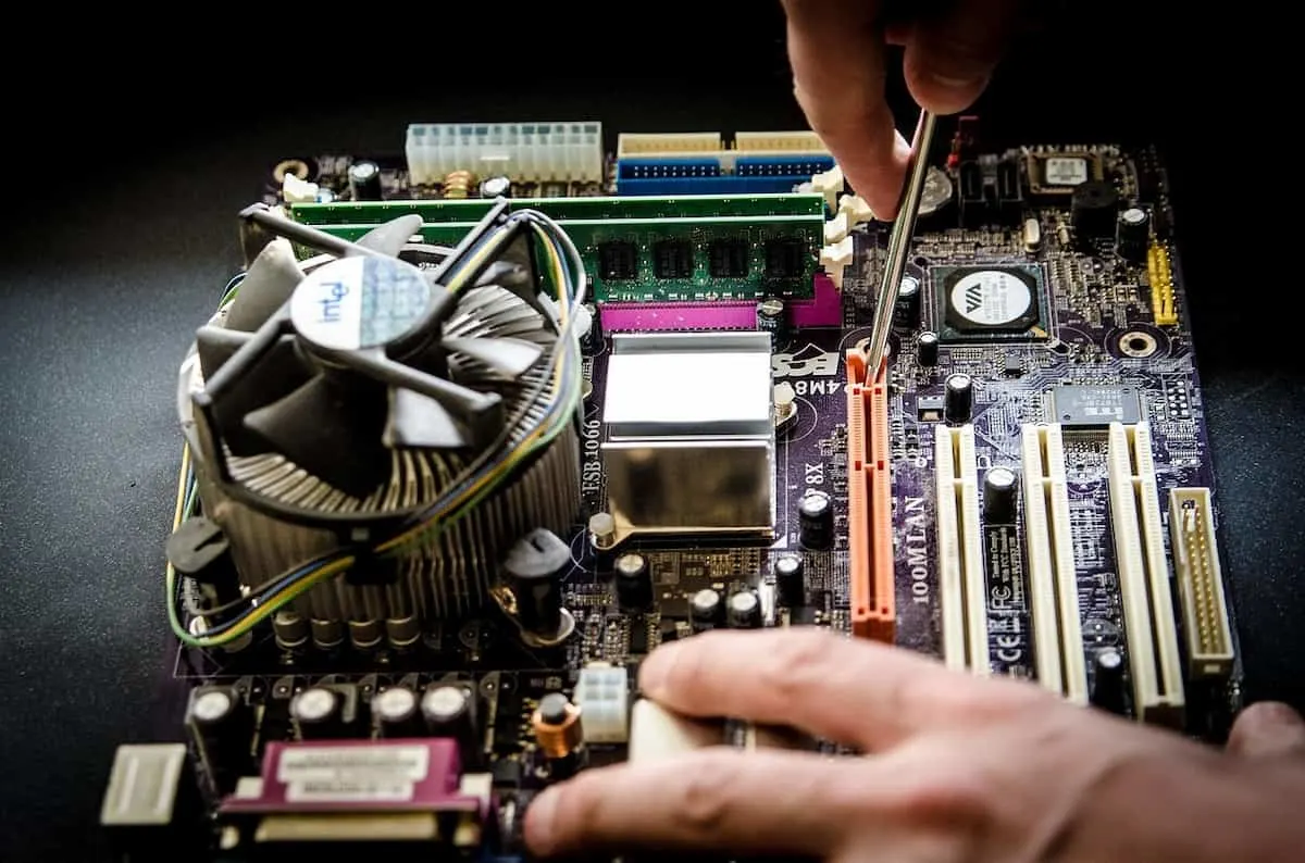 Mano manipulando una placa base de PC con un destornillador.