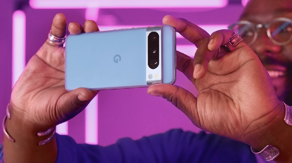 Un hombre sostiene un teléfono azul claro horizontalmente con dos manos adornadas con anillos y pulseras plateadas.