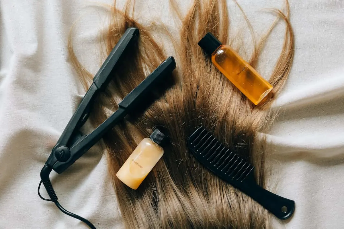 Plancha de pelo, productos capilares y cepillo sobre una melena rubia.