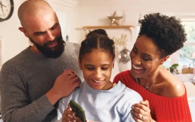 Familia sonriente reunida en una cocina. La hija mira un teléfono. Burbuja de texto: "Privacidad en redes sociales activada".