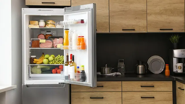 Refrigerador abierto lleno de alimentos en una cocina con gabinetes de madera y electrodomésticos.