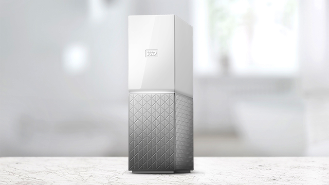 Un disco duro externo con la parte superior blanca y la inferior plateada con un patrón de rombos en una mesa blanca.