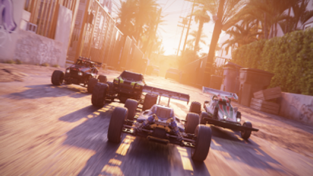 Carrera de coches en calle con edificios y vegetación. Los vehículos tienen ruedas grandes y alerones. El sol brilla al fondo.