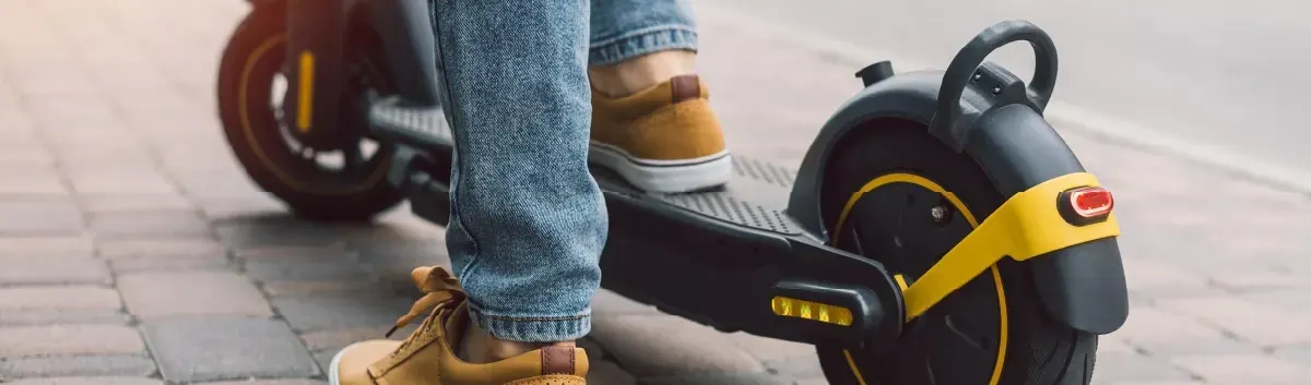 Persona conduciendo un patinete eléctrico por la acera.