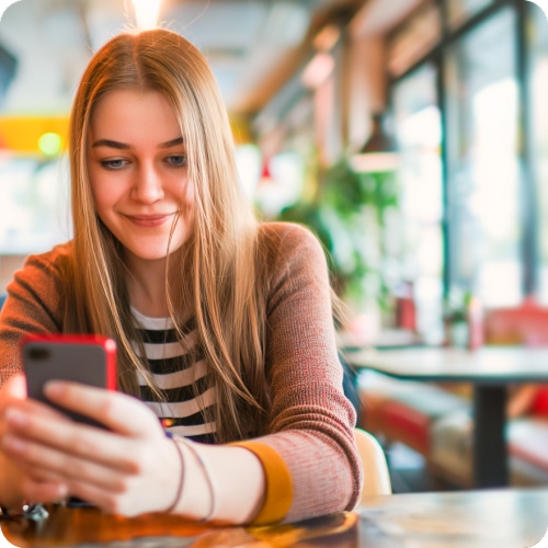 Una persona usa un móvil. Hay un anuncio con texto sobre detección de fraudes por SMS. Fondo difuminado de interior con plantas.