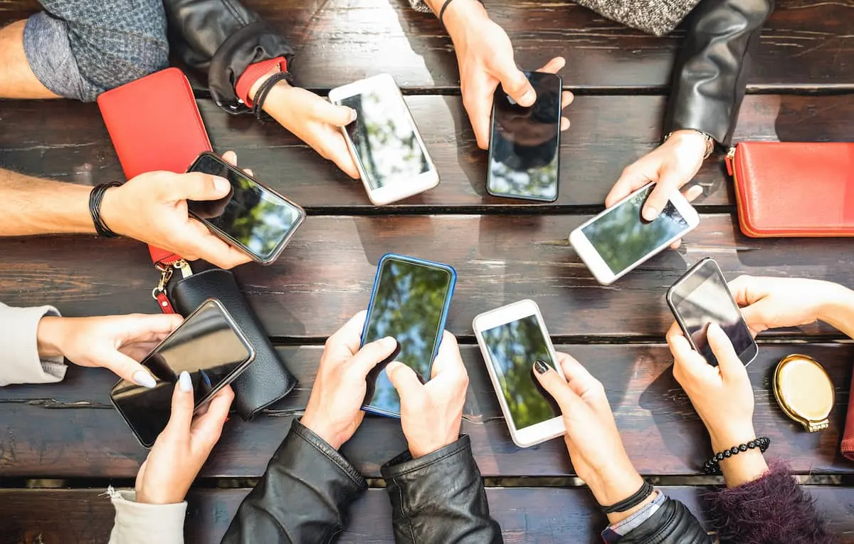 Vista superior de un grupo de personas sosteniendo smartphones sobre una mesa de madera.