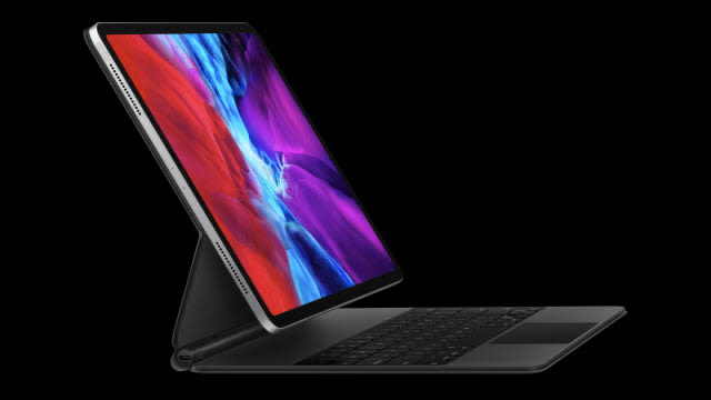 Tablet gris con pantalla iluminada mostrando rojo, azul y morado, conectada a un teclado negro sobre fondo negro.