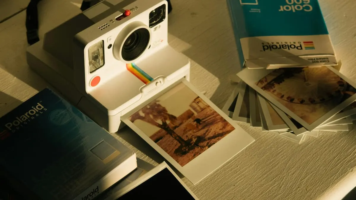 Cámara Polaroid blanca imprimiendo una foto junto a varias instantáneas y cajas de película.