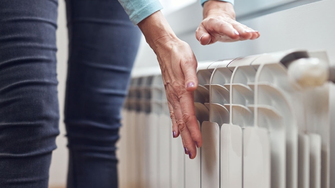 Una persona con pantalones azules toca un radiador blanco con ambas manos.