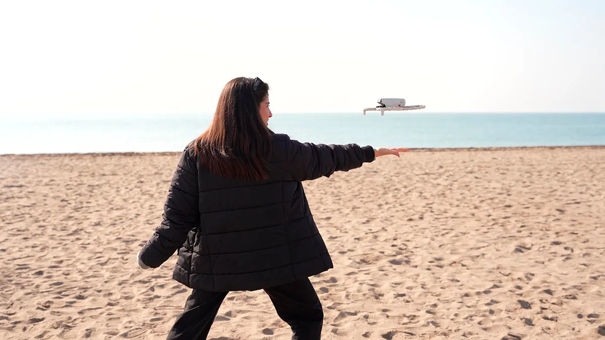 Mujer lanzando un dron DJI Flip en la playa, capturando un momento de vuelo junto al mar.