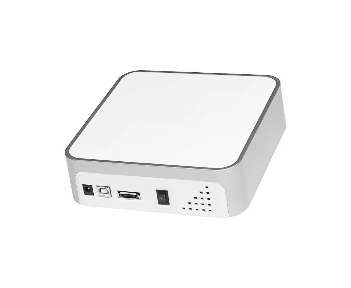 Pequeño mini PC blanco con varios puertos en la parte frontal sobre fondo blanco.