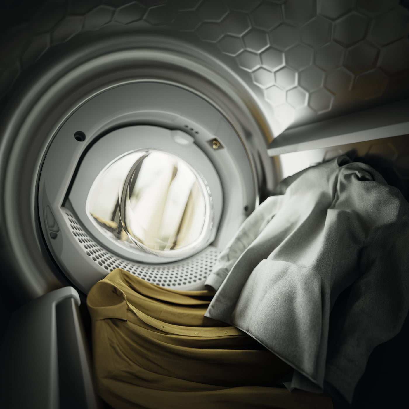 Vista interior de una secadora con ropa amarilla y blanca. La pared trasera tiene un diseño hexagonal.