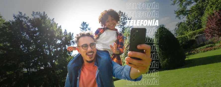 Padre e hijo sonríen mientras se toman una selfie al aire libre. Fondo verde y la palabra “Telefonía” repetida.
