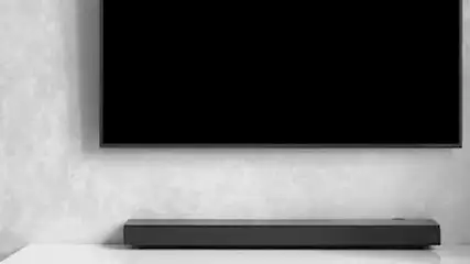 En una habitación gris y blanca, un televisor negro está montado sobre una barra de sonido horizontal.