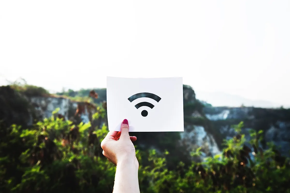 Mano sosteniendo papel blanco con símbolo wifi negro, con fondo de vegetación y formaciones rocosas.