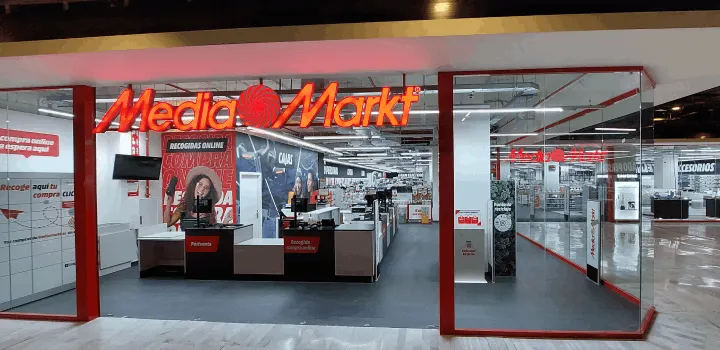 Entrada a tienda Media Markt con letrero naranja. Se ven cajas registradoras y pasillos con productos en venta.