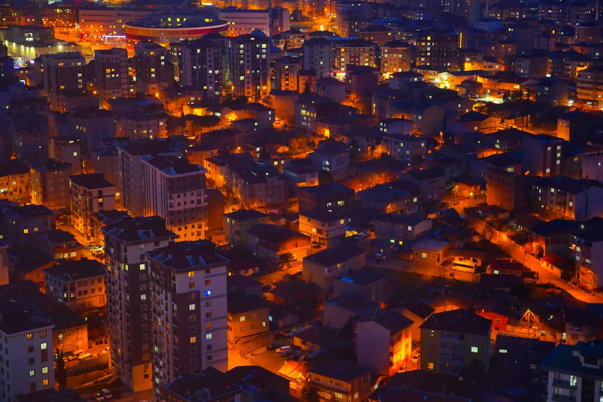 Vista aérea nocturna de una ciudad con edificios y calles iluminadas por luces anaranjadas.