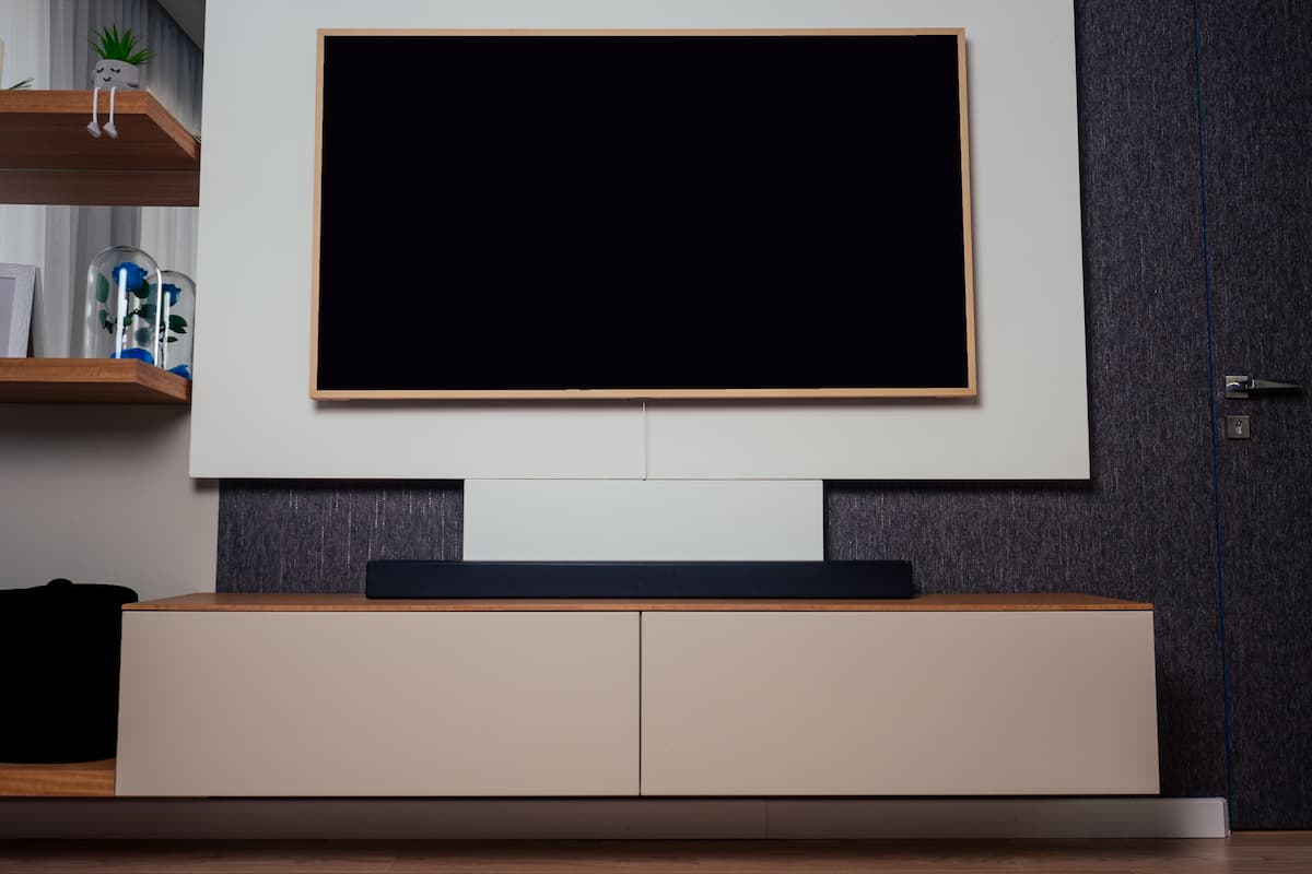 Barra de sonido colocada debajo de un televisor grande en un salón moderno con mueble bajo y estanterías de madera