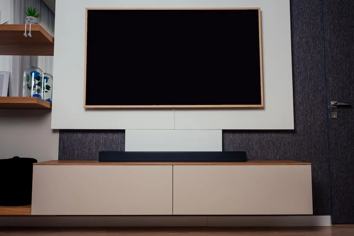 Barra de sonido colocada debajo de un televisor grande en un salón moderno con mueble bajo y estanterías de madera