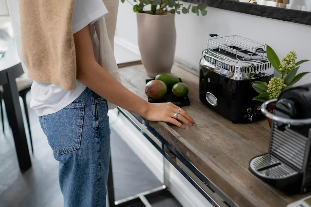 Persona en cocina junto a una tostadora y una cafetera.