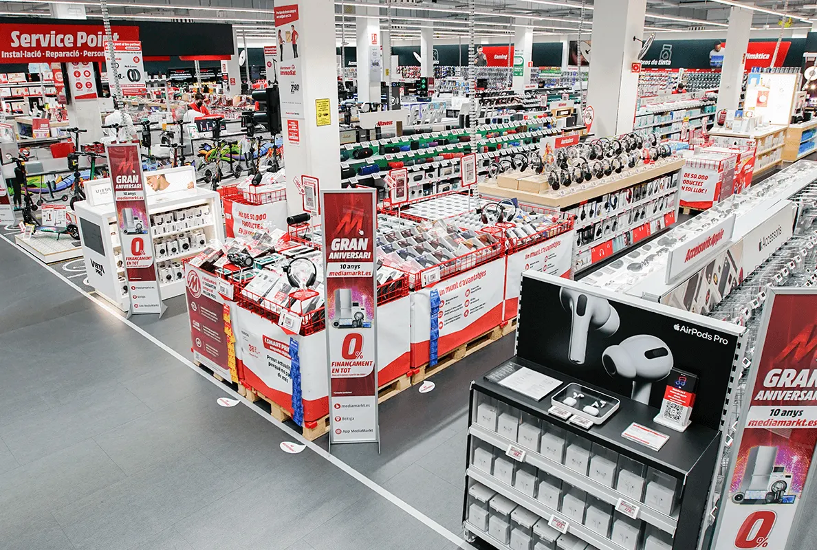 Vista de un centro comercial con pasillos llenos de estantes de productos electrónicos y carteles promocionales.