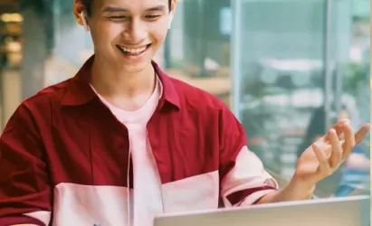 Un hombre sonríe mientras usa una laptop. Un mensaje flotante indica que una VPN está activada con una marca de verificación verde.