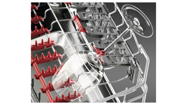 Primer plano del interior de un lavavajillas con soportes rojos y grises que sostienen firmemente una copa de vino transparente.