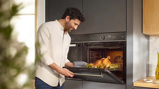 Un hombre extrae la bandeja del horno y puede verse como está iluminado y pueden verse los alimentos perfectamente.