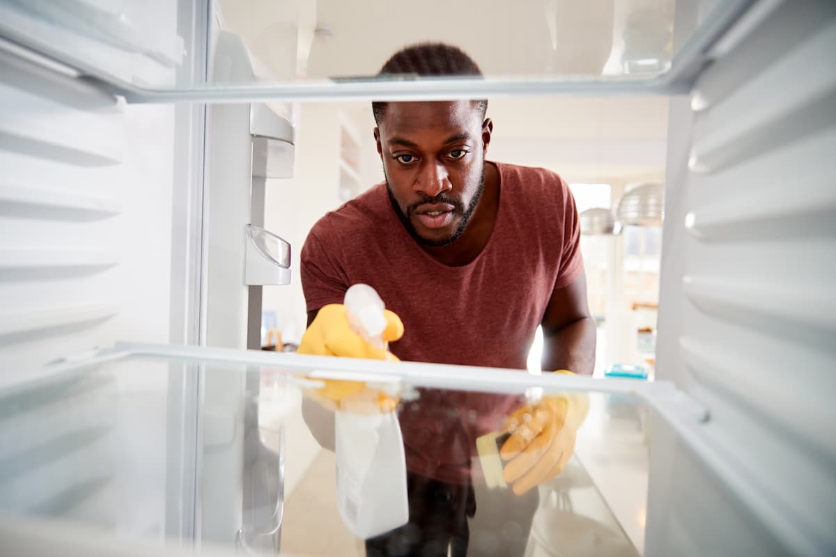 Hombre limpiando el interior de un refrigerador con un paño y guantes amarillos
