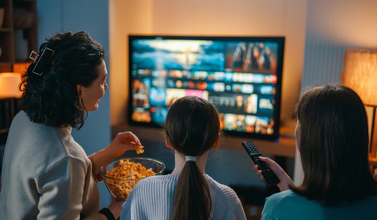 Familia viendo una plataforma de streaming en televisor con palomitas y control remoto