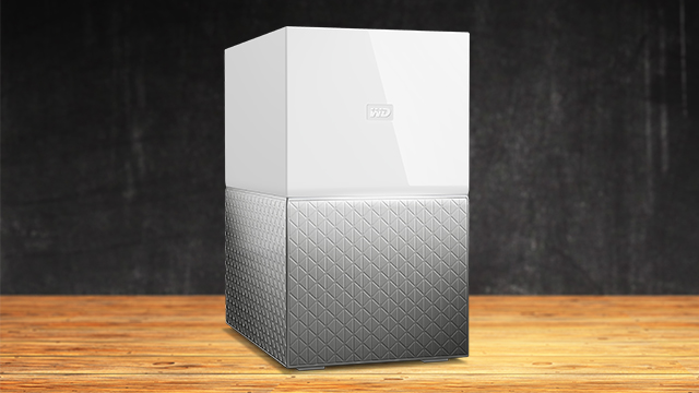 Caja blanca con logo en la parte superior y base gris con diseño de diamantes sobre mesa de madera contra un fondo oscuro.