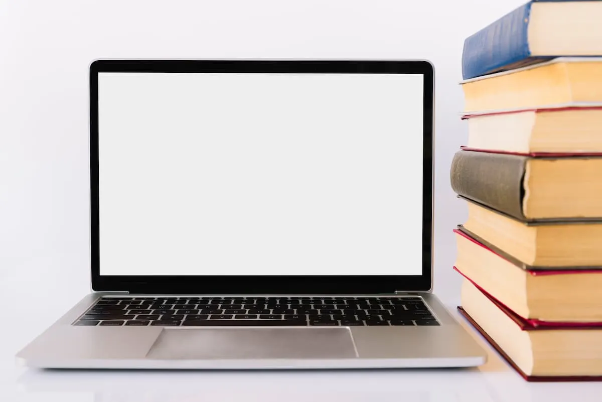Ultrabook con pantalla en blanco junto a una pila de libros.