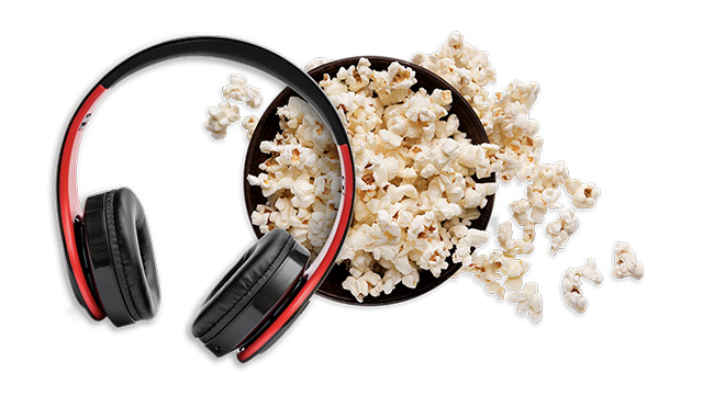 Audífonos negros y rojos junto a un tazón negro lleno de palomitas de maíz sobre un fondo blanco.