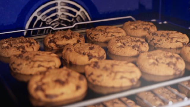 Galletas horneándose en bandeja metálica dentro de horno azul con rejilla protectora blanca visible.