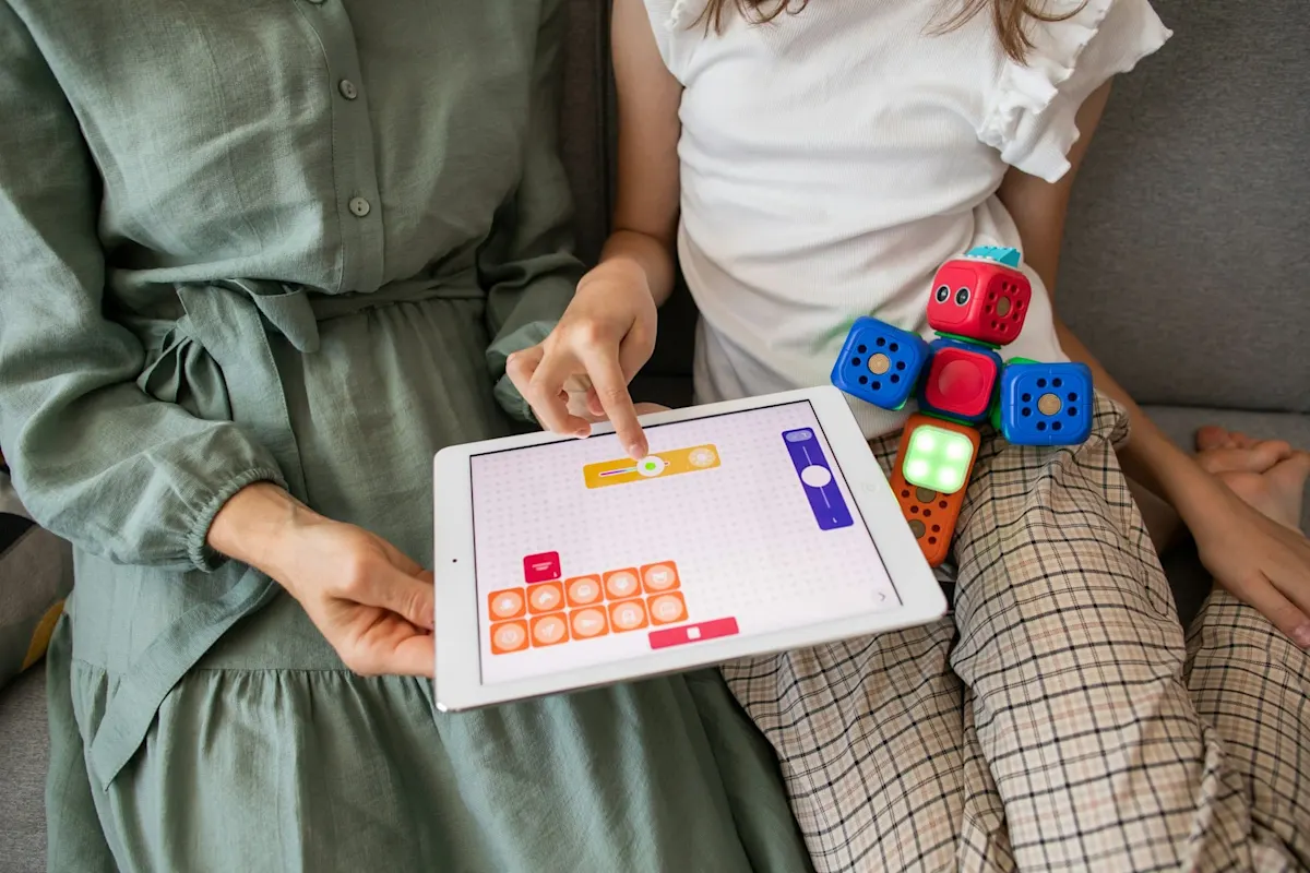 Dos personas sentadas en un sofá usando una tableta y jugando con cubos de colores.